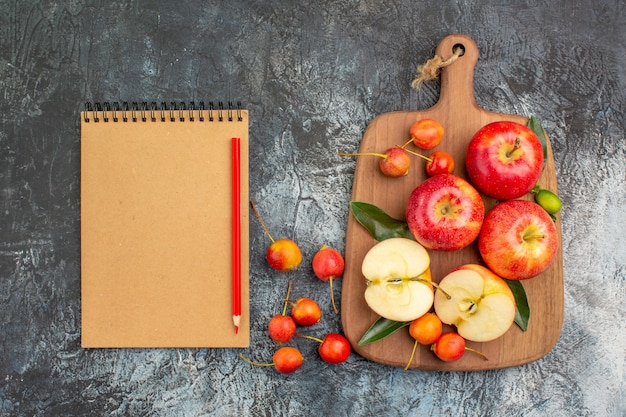 Foto gratuita vista superior manzanas la tabla de cortar con lápiz de cuaderno de cerezas de manzanas