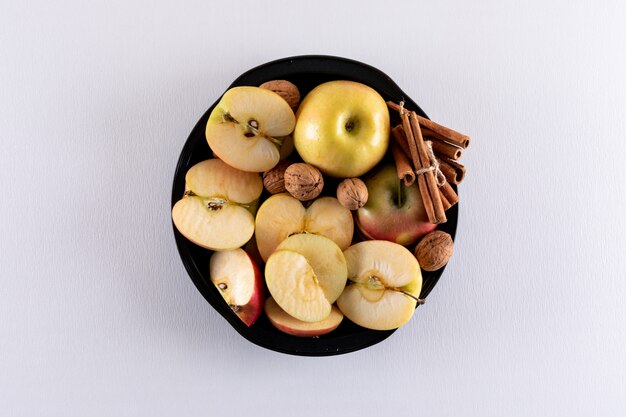 Vista superior de manzanas en un tazón negro con nueces de canela en blanco horizontal