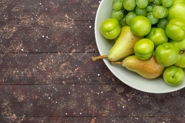 Vista superior de manzanas y uvas junto con peras y ciruelas cereza dentro de la placa en el fondo rústico de madera fruta dulce meloso