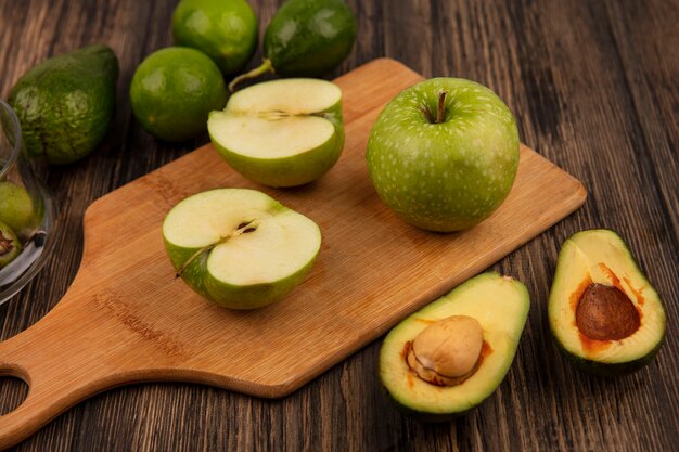 Vista superior de manzanas verdes frescas en una tabla de cocina de madera con aguacates y limas aislado en una pared de madera