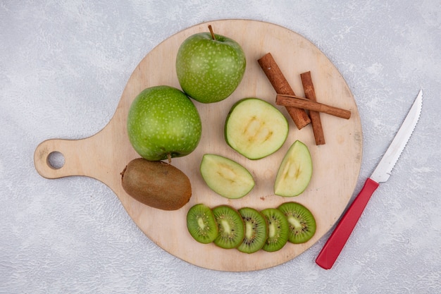 Foto gratuita vista superior de manzanas verdes con rodajas de kiwi y canela en un soporte con un cuchillo sobre un fondo blanco.