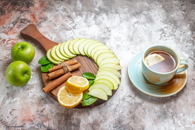 Vista superior de manzanas verdes en rodajas con una taza de té y limones sobre fondo claro