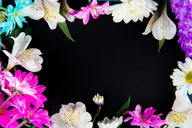 Vista superior de un marco de flores de alstroemeria de color blanco con flores de crisantemo de color rosa y blanco sobre fondo negro con espacio de copia