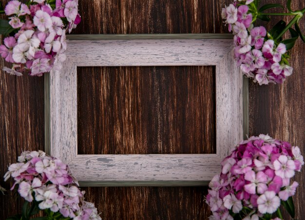 Vista superior del marco gris con flores de color rosa claro sobre una superficie de madera