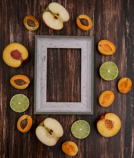 Vista superior del marco gris con rodajas de limón melocotón albaricoques y manzana sobre una superficie de madera