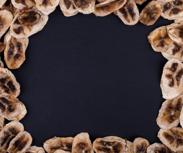 Vista superior de un marco hecho de chips de plátano secos dispuestos sobre fondo negro con espacio de copia