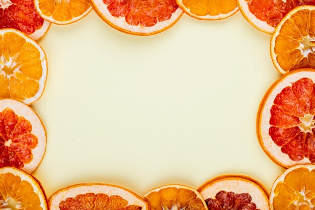 Vista superior de un marco hecho de rodajas secas de naranja y pomelo dispuestas sobre fondo blanco con espacio de copia
