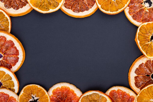 Vista superior de un marco hecho de rodajas secas de naranja y pomelo dispuestas sobre fondo negro con espacio de copia