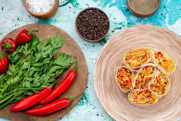 Vista superior más cercana de la masa de rollos de verduras en rodajas con relleno sabroso junto con verduras y pimientos rojos picantes en el escritorio azul brillante