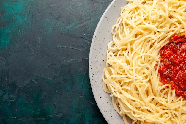 Vista superior más cercana pasta italiana cocida con carne picada y salsa de tomate en la superficie azul oscuro