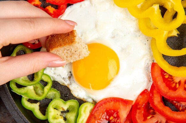 Vista superior más cercana sabrosa tortilla con tomates y pimientos en rodajas sobre una superficie oscura