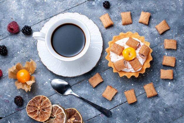 Vista superior más cercana de la taza de café con pastel cremoso almohada formada galletas junto con bayas en escritorio gris