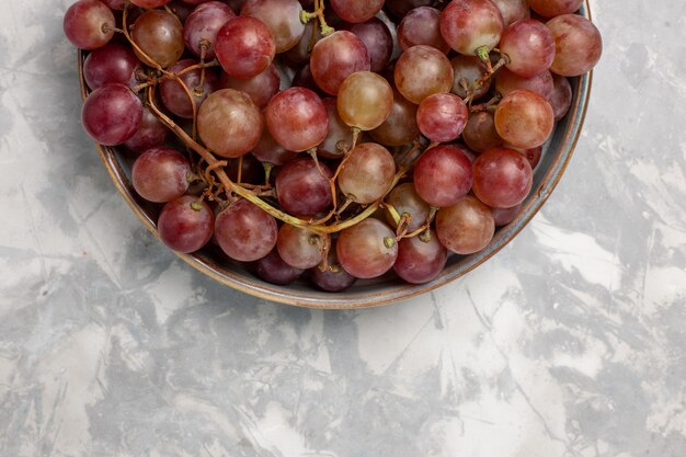 Vista superior más cercana uvas rojas frescas jugosas frutas dulces suaves en el escritorio de color blanco claro fruta fresca jugo suave vino