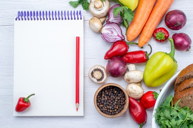 Vista superior más cercana de verduras frescas como cebollas, zanahoria y pimiento con pan en la mesa de luz