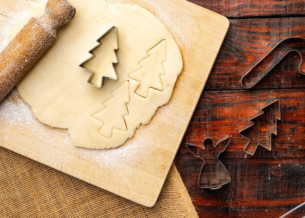 Vista superior de la masa cruda y cortadores de galletas de Navidad en la mesa de la cocina rústica