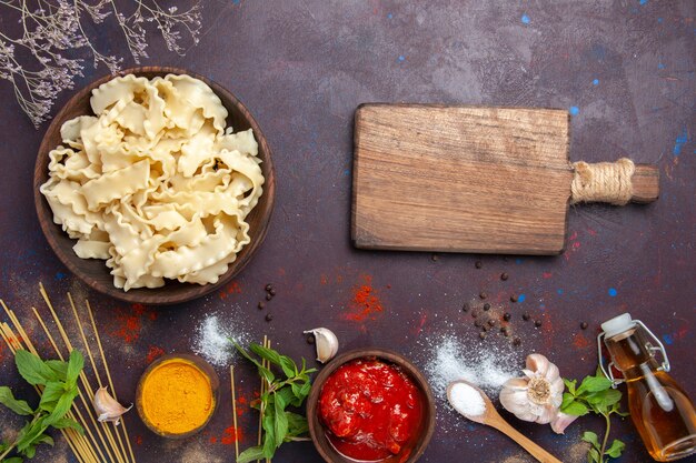 Vista superior de masa cruda en rodajas con salsa de tomate sobre fondo oscuro, cena, pasta, masa