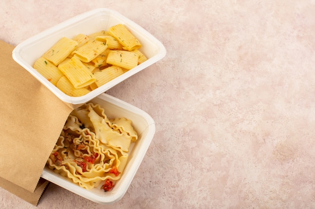 Una vista superior de masa y pasta italiana con tomates y carne dentro de tazones blancos y paquete en rosa