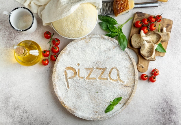 Vista superior de la masa de pizza con champiñones y tomates y palabra escrita en harina