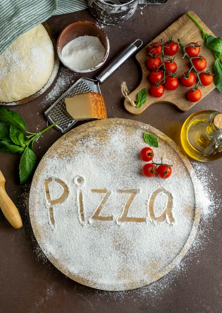 Vista superior de la masa de pizza con tablero de madera y palabra escrita en harina