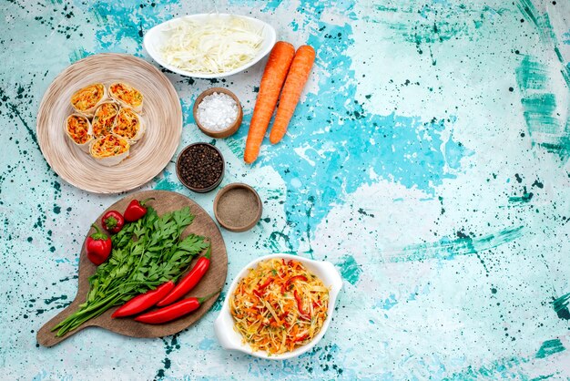 Vista superior de la masa de rollos de verduras en rodajas con un relleno sabroso junto con zanahorias verdes y pimientos rojos picantes en el escritorio de color azul brillante.