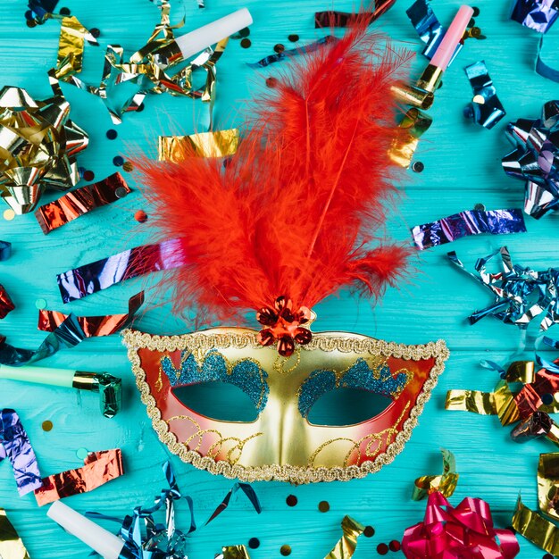 Vista superior de la máscara de carnaval veneciano con plumas en oro y rojo con material de decoración de fiesta