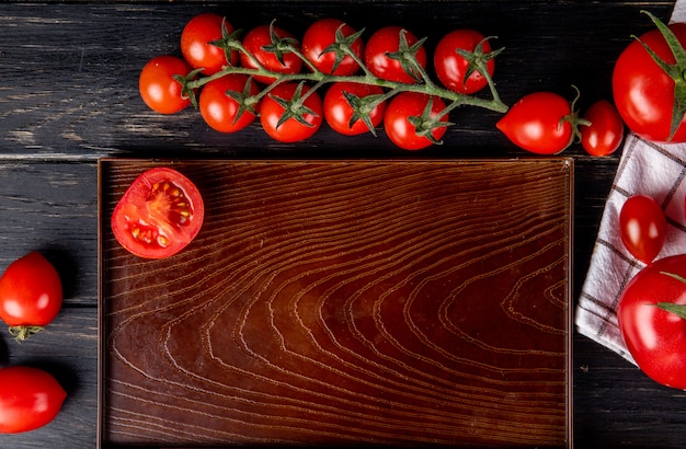 Vista superior de medio tomate cortado en bandeja y enteros sobre superficie de madera