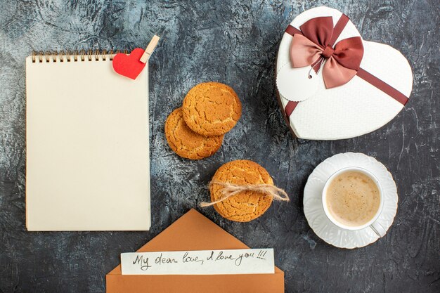 Vista superior de la mejor sorpresa con un hermoso sobre de cajas de regalo con la letra una taza de galletas de café para un ser querido en una superficie oscura helada