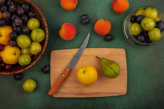 Vista superior de melocotón amarillo sobre una tabla de cocina de madera con pera verde con cuchillo sobre un fondo verde