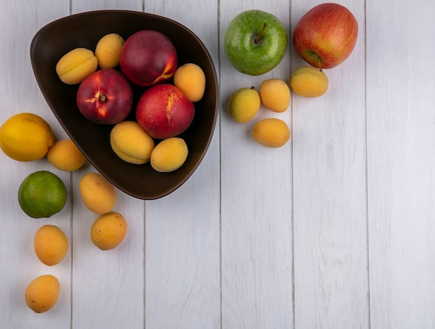 Vista superior de melocotones con albaricoques en un recipiente con manzanas sobre una superficie blanca