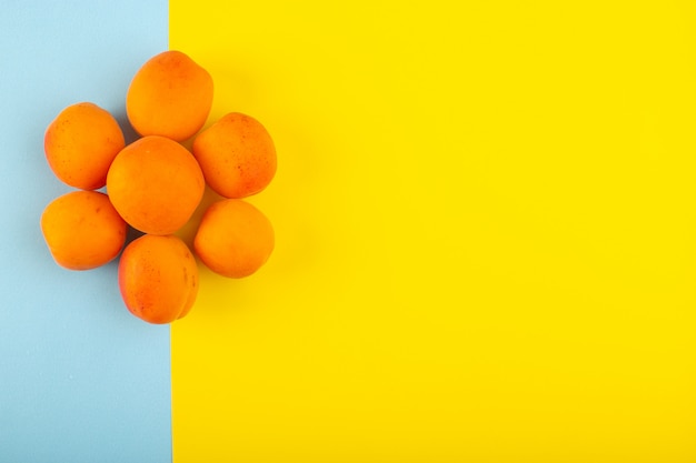 Una vista superior de melocotones naranjas amargos y sabrosos fetos frescos forrados en el fondo azul-amarillo de frutas exóticas jugo de verano