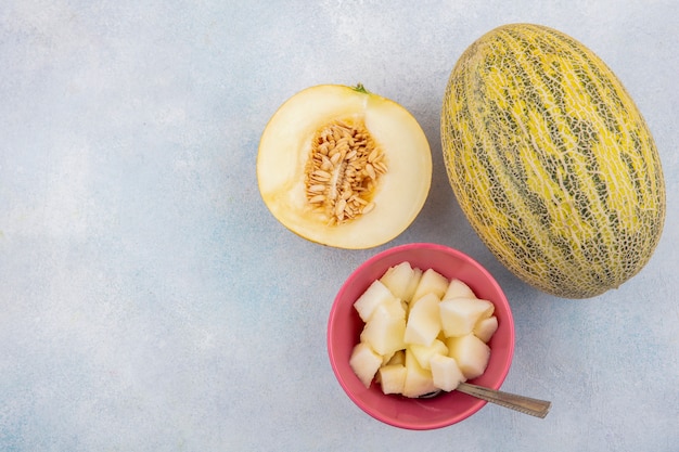 Vista superior de melón cantalupo con rodajas en un tazón rosa sobre blanco