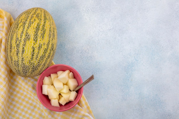 Vista superior del melón con rodajas en un tazón rosa sobre mantel amarillo sobre superficie blanca