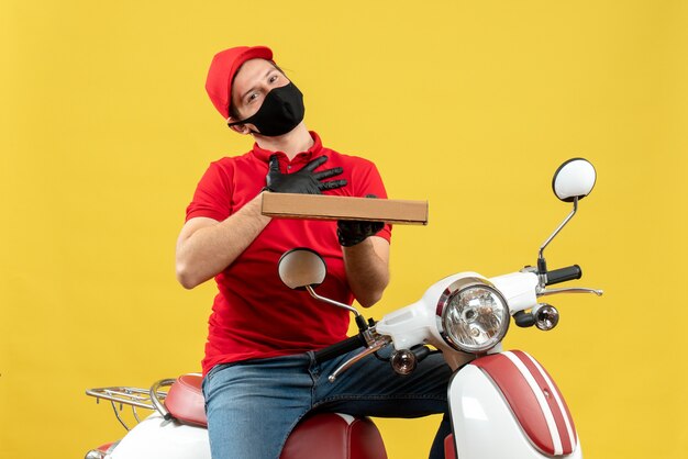 Foto gratuita vista superior del mensajero agradecido con blusa roja y guantes de sombrero en máscara médica sentado en scooter mostrando orden