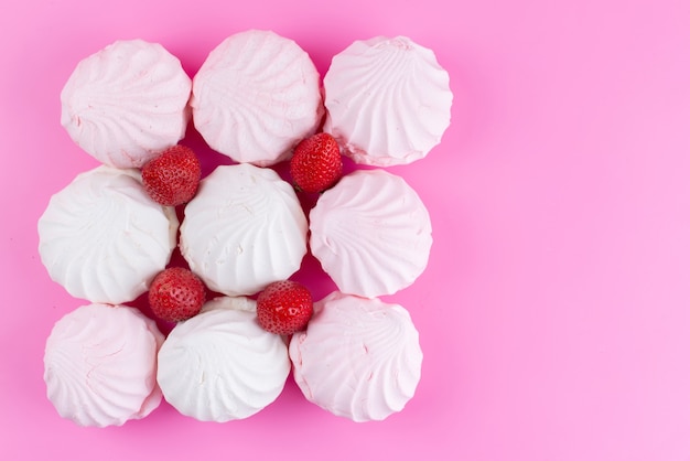 Una vista superior de merengues blancos con fresas rojas frescas forradas en rosa escritorio, confitería de galleta dulce color azúcar