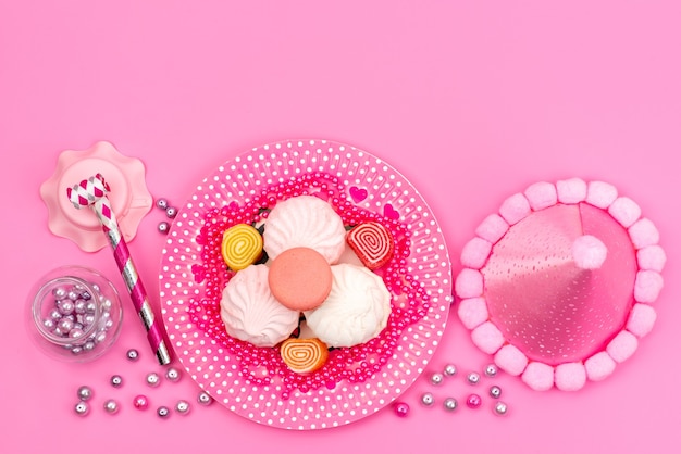 Una vista superior de merengues y mermeladas coloridas junto con un silbato de cumpleaños y un collar en rosa, pastel de azúcar dulce