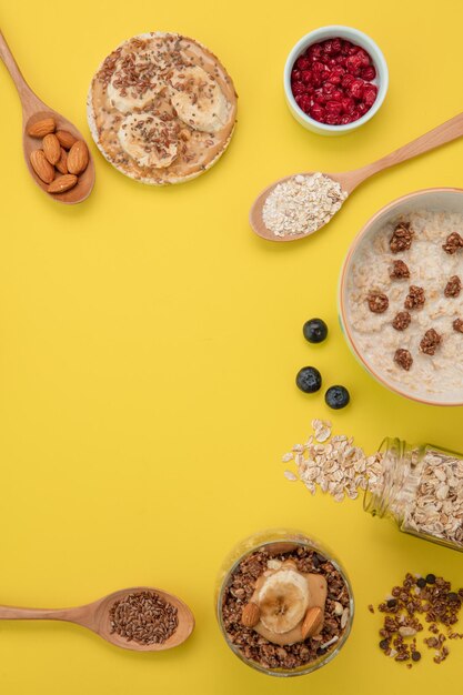 Vista superior de la merienda de pan crujiente de plátano, avena y leche de nuez y batido de almendras y nueces de plátano con cucharas de endrino de grosella roja llenas de semillas de chía y almendras sobre fondo amarillo