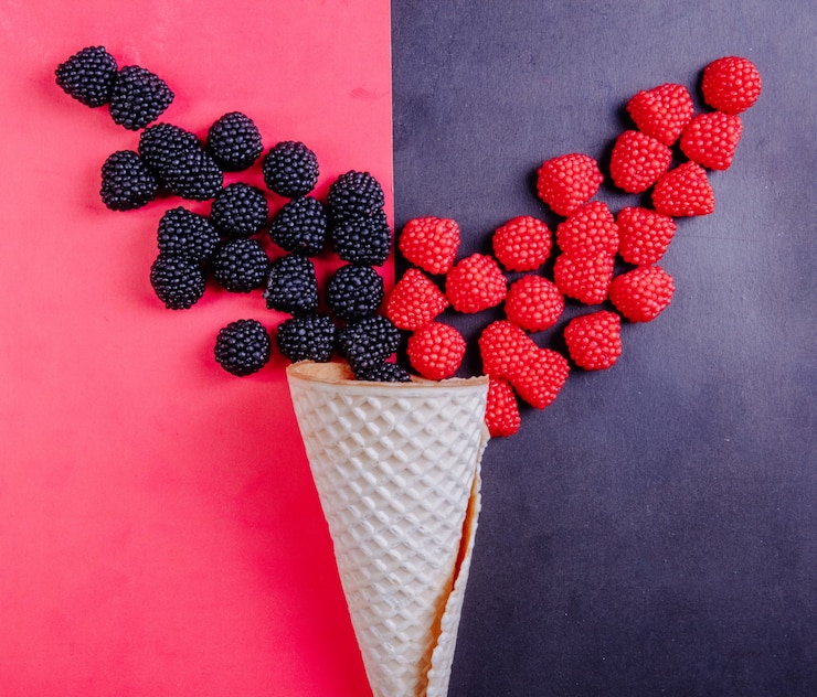 Foto gratuito vista superior de mermelada en forma de frambuesas sobre un fondo negro y moras sobre un fondo rojo con un cono de waffle
