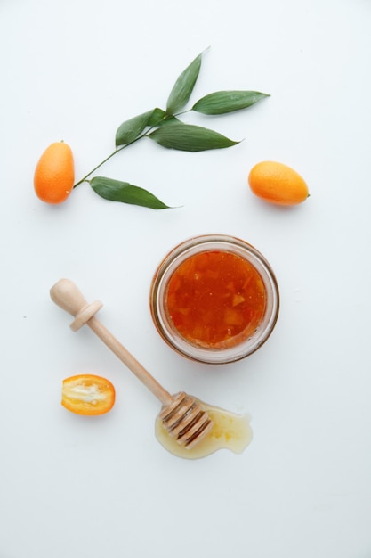 Vista superior de mermelada de membrillo en frasco de vidrio y kumquats con cazo de mermelada sobre fondo blanco