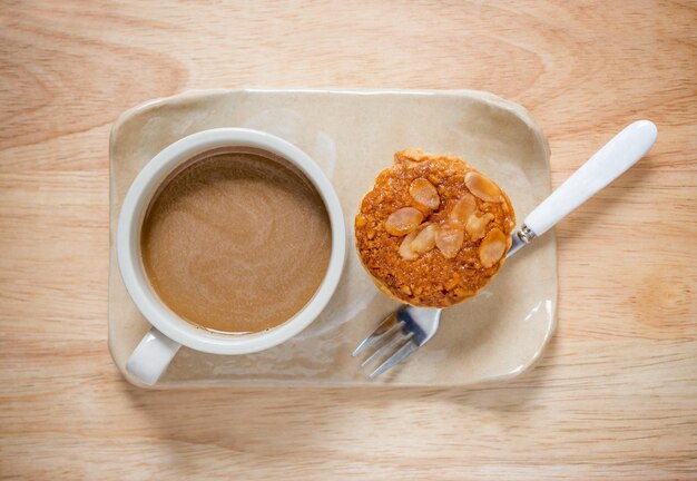 Vista superior de la mesa de café caliente y pastel de taza de almendras de café sobre fondo de mesa de madera