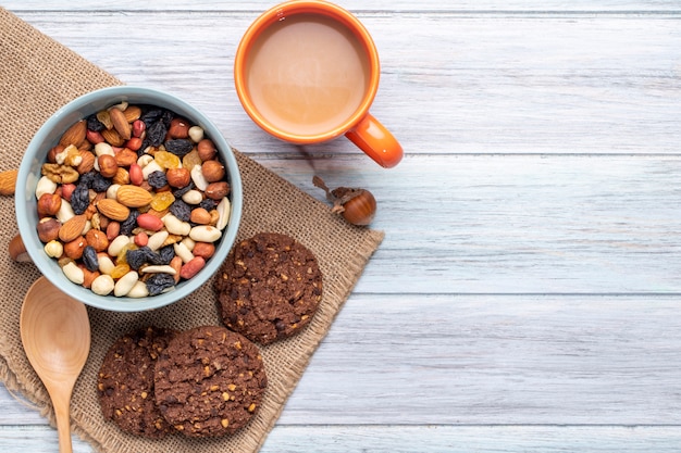 Vista superior de la mezcla de nueces y frutas secas en un tazón y galletas de avena con una taza de bebida de cacao en rústico