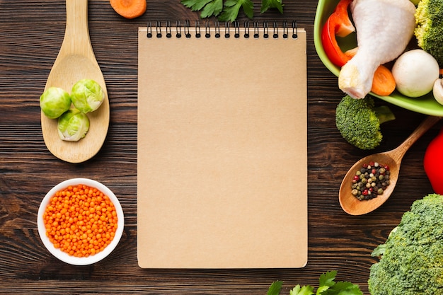 Vista superior mezcla de verduras y muslo de pollo en un tazón con cuaderno en blanco