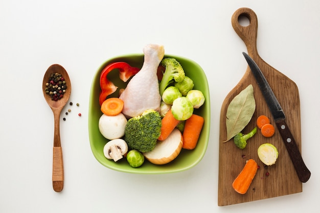 Vista superior mezcla de verduras en la tabla de cortar y en un tazón con muslo de pollo y cuchara