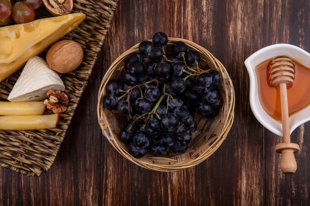 Vista superior de la miel en un platillo con uvas variedades de quesos y nueces en un soporte sobre un fondo de madera