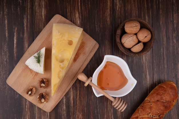 Vista superior de la miel en un platillo con una variedad de quesos en un soporte con nueces y una hogaza de pan sobre un fondo de madera