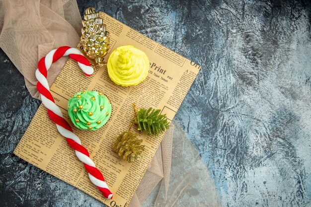 Vista superior mini cupcakes dulces de Navidad adornos de Navidad en un mantón de periódico beige sobre una superficie oscura