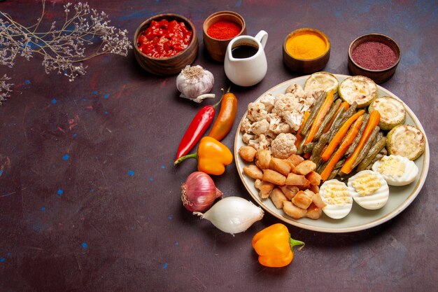 Vista superior de la mitad de la deliciosa comida de huevo con verduras cocidas y condimentos en el espacio oscuro