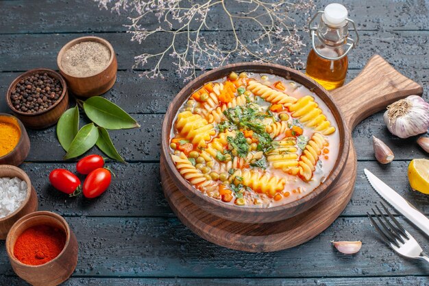 Vista superior de la mitad de la deliciosa sopa de pasta de pasta italiana en espiral con condimentos en el escritorio azul oscuro sopa de pasta plato de color cena cocina