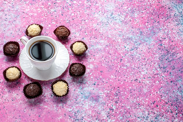 Vista superior de la mitad de los deliciosos caramelos de chocolate chocolate blanco y negro con una taza de té sobre fondo rosa.