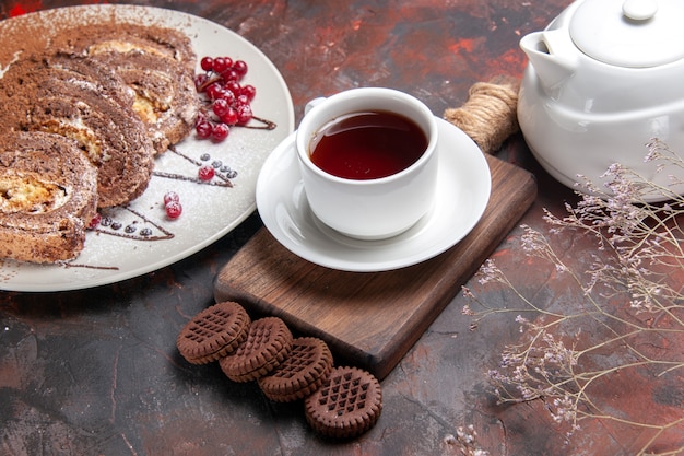 Vista superior de la mitad de deliciosos rollos de galletas con galletas y té en la mesa oscura pastel de pastel de dulces