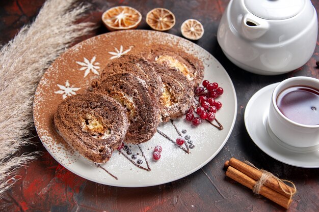 Vista superior de la mitad de deliciosos rollos de galletas con una taza de té en la mesa oscura pastel de té pastel dulce